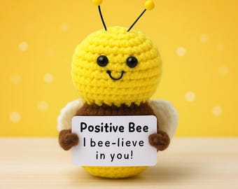 Może przedstawiać: Szydełkowa żółta pszczoła z czarnymi oczami, uśmiechniętymi ustami i antenkami. Pszczoła trzyma znak z napisem "Positive Bee I bee-lieve in you!" na żółtym tle. Pszczoła ma brązowe i białe skrzydła.