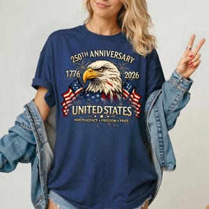 May include: Navy blue t-shirt featuring a detailed graphic of an American bald eagle with the text "250th Anniversary 1776-2026 United States Independence Freedom Pride". The design includes American flags and fireworks.