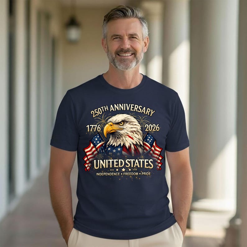 May include: Navy blue t-shirt with a graphic of an American bald eagle, flags, and the text "250th Anniversary 1776-2026 United States Independence Freedom Pride". The shirt is worn by a person.