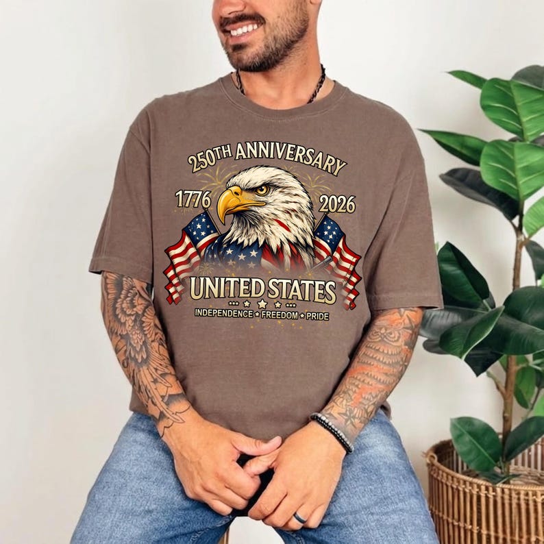 May include: Brown t-shirt featuring a detailed graphic of an American bald eagle with the text "250th Anniversary 1776-2026 United States Independence Freedom Pride" and two American flags. The shirt is a casual style.
