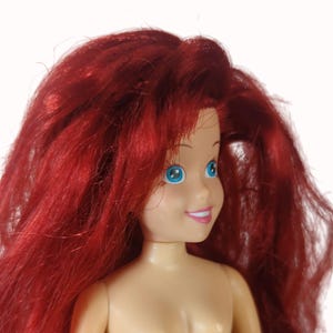 Peut inclure: Poup&eacute;e &agrave; la peau claire, aux yeux bleus et &agrave; l'expression souriante. La poup&eacute;e a de longs cheveux roux vibrants. La poup&eacute;e est un personnage d'un film d'animation populaire. La poup&eacute;e est un objet de collection.