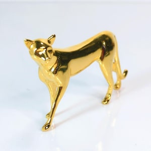 May include: A gold-colored figurine of a cat in a standing pose. The cat is sleek and stylized, with its head turned slightly to the side. The figurine has a glossy finish and is set against a white background.
