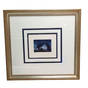 May include: Framed artwork featuring a silhouette of two cats facing each other under a starry night sky with a crescent moon. The artwork is matted in white and navy blue, set within a gold-colored frame.