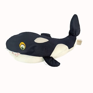 May include: A plush orca whale toy in black and white with a smiling face and a small fin. The toy has a tag on the side. The orca has a white belly and white patches on its body.