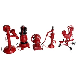 May include: A collection of five miniature cast iron decorative items painted in bright red. The set includes a vintage-style telephone, a small stove, a coffee grinder, a water pump, and a rooster weather vane, each with thin red hanging cords.