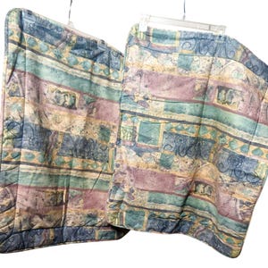 May include: Two pillowcases with a colorful, abstract pattern. The design features horizontal stripes in shades of blue, green, purple, and tan. The pillowcases are hanging on clear plastic hangers against a white background.