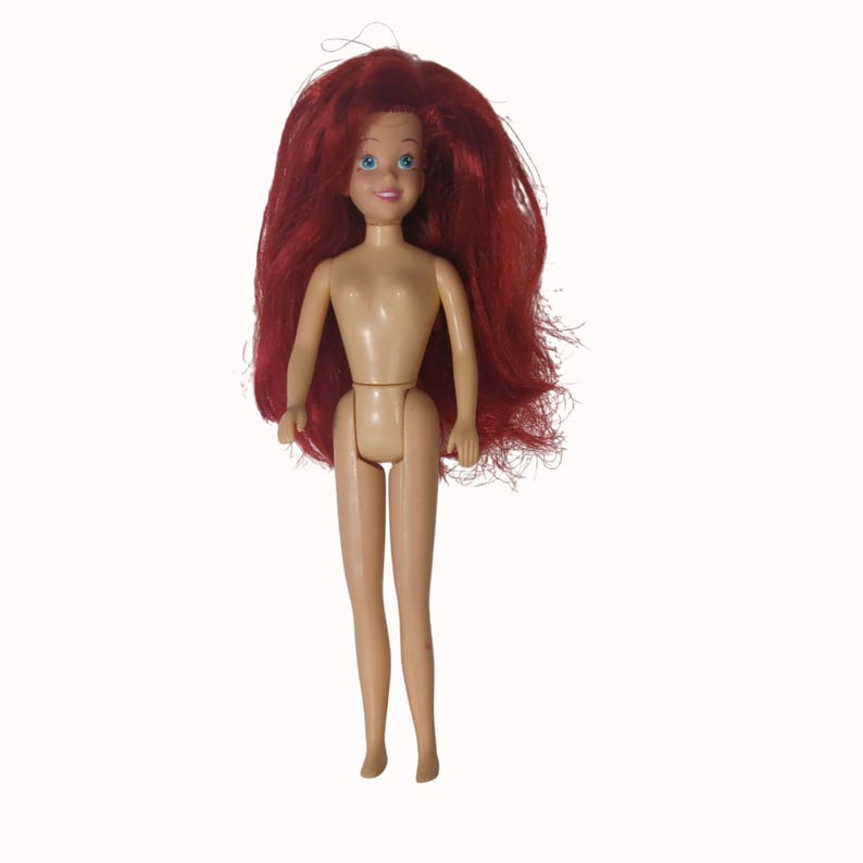 Peut inclure: Une poup&eacute;e vintage avec de longs cheveux roux vifs et des yeux bleus. La poup&eacute;e a un teint h&acirc;l&eacute; et n'est pas v&ecirc;tue. Les bras de la poup&eacute;e sont tendus et ses jambes sont droites. La poup&eacute;e est sur fond blanc.
