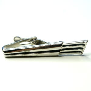 May include: A silver-toned metal tie clip featuring a sleek, elongated design with three parallel black horizontal stripes near the tapered end. The accessory includes a spring-loaded hinge mechanism on the back for securing it to a necktie.