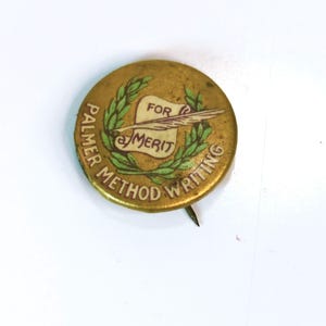 May include: A vintage, round, brass-colored pin with the text "PALMER METHOD WRITING" around the edge. The center features a scroll, quill, and the words "FOR MERIT" within a laurel wreath.