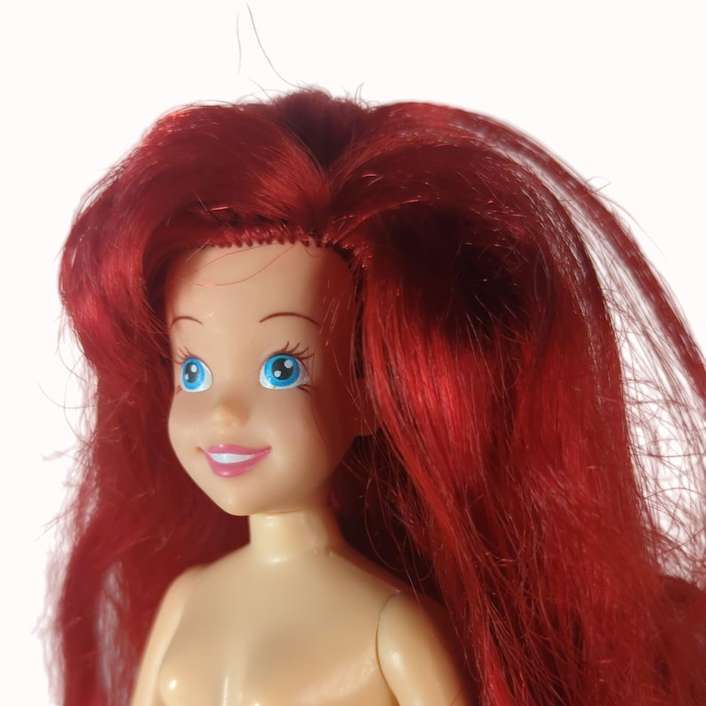 Peut inclure: Gros plan sur une poup&eacute;e aux cheveux roux et aux yeux bleus. La poup&eacute;e a le teint clair et un l&eacute;ger sourire. Les cheveux de la poup&eacute;e sont longs et fluides, et les yeux sont grands et expressifs. La poup&eacute;e est un personnage populaire d'un film pour enfants.