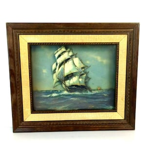 May include: A framed painting of a ship with white sails sailing on a blue ocean. The painting is in a brown wooden frame with a gold inner border.