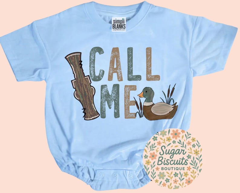May include: Pale blue baby bodysuit featuring the words "CALL ME" in green, brown, and tan. The design includes a cartoon duck and a brown hunting call. The bodysuit is from Simpli Blanks.