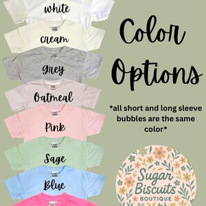 May include: A selection of t-shirts in shades such as white, cream, grey, oatmeal, pink, sage, blue, and neon pink. Each shirt displays its colour name. The image also includes the words "Color Options" and the Sugar Biscuits Boutique logo.