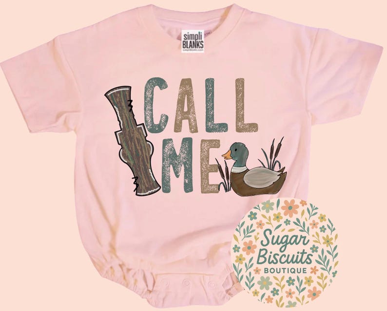 May include: A pale pink baby bodysuit featuring the text "CALL ME" in green and brown. The design includes a duck and a duck call. The bodysuit has short sleeves and a round neckline.