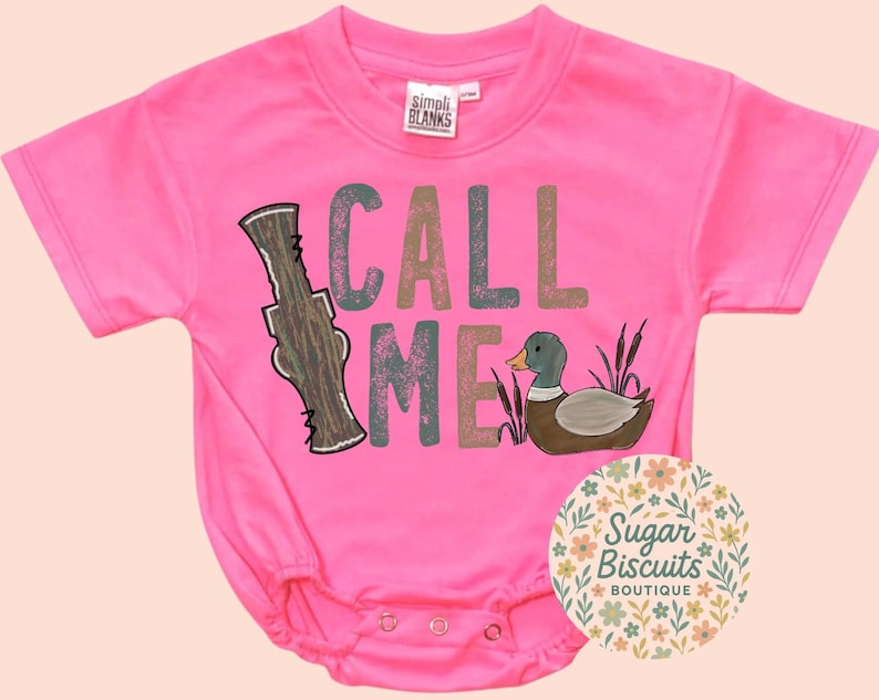 May include: A vibrant pink baby bodysuit featuring the text "CALL ME" in various colours and a duck illustration. The bodysuit has short sleeves and popper fastenings. The label "SIMPLI BLANKS" is visible.