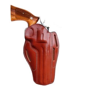 May include: A brown leather holster for a handgun. The holster has a stitched design and a flap that covers the trigger guard.
