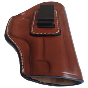 May include: A brown leather holster with a black clip. The holster has white stitching around the edges.
