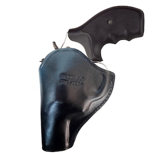 Puede incluir: Una funda de cuero negra con un clip de metal plateado y el texto "Daytona Holsters" grabado en el lateral. Una pistola negra es parcialmente visible en la funda.