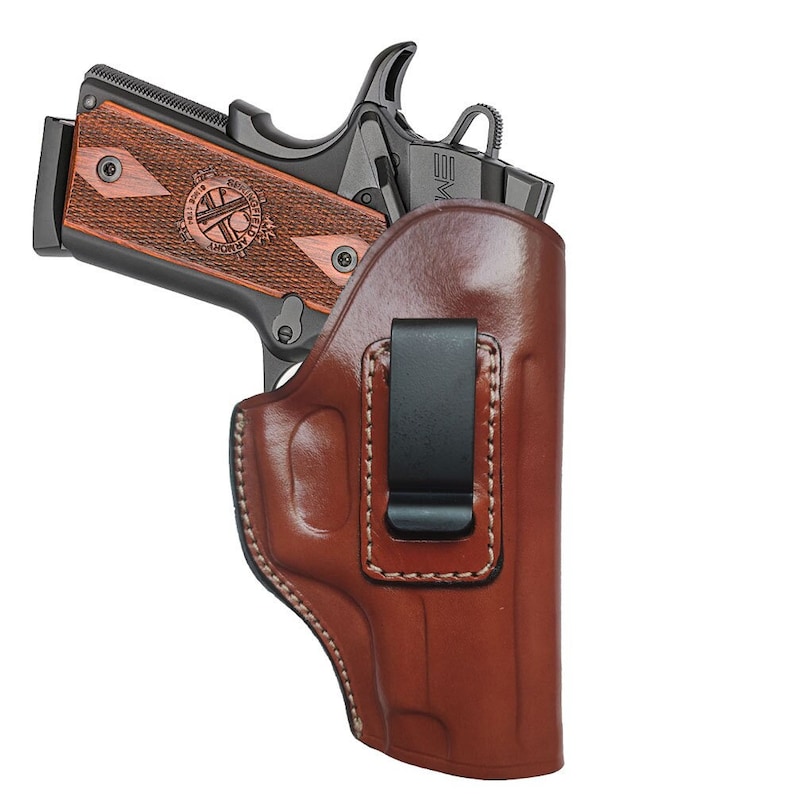 May include: A brown leather holster with a black clip for a handgun. The holster has a stitched design and is made of high-quality leather.