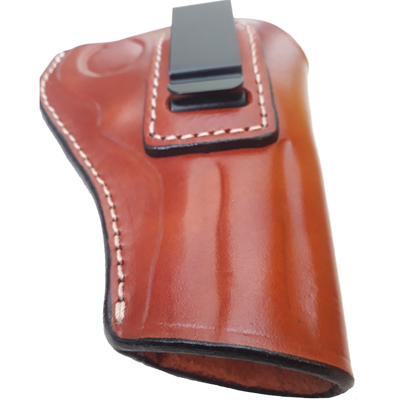 Puede incluir: Una funda de cuero marr&oacute;n con un clip negro. La funda tiene costuras blancas alrededor de los bordes.