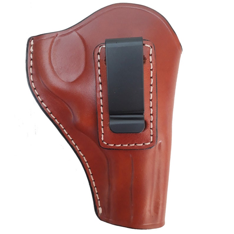 Puede incluir: Una funda de cuero marr&oacute;n con un clip de metal negro. La funda tiene costuras blancas alrededor de los bordes.