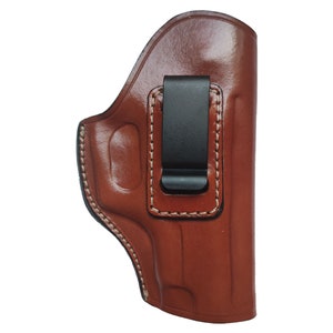 May include: A brown leather holster with a black metal clip. The holster has a stitched edge and is designed to hold a handgun.