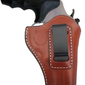 Könnte beinhalten: Ein braunes Lederholster mit einem Clip für eine Pistole. Das Holster hat weiße Nähte und eine glatte, braune Lederoberfläche.