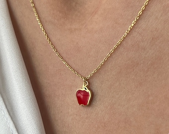May include: A gold chain necklace with a red enamel apple pendant.