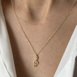 Pu&ograve; includere: Una collana con catena dorata con un piccolo ciondolo a forma di chiave di violino scintillante. Il ciondolo &egrave; decorato con piccole pietre trasparenti.