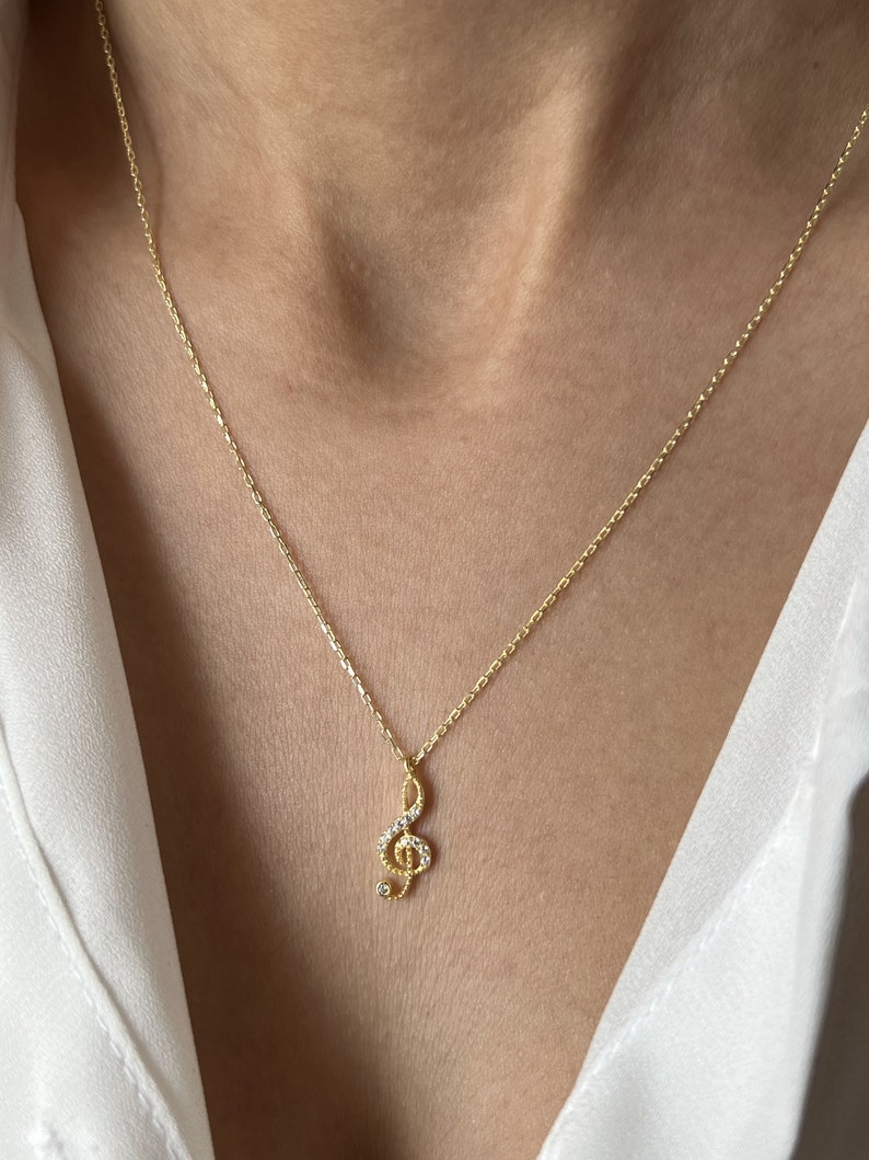 Pu&ograve; includere: Una collana con catena dorata con un piccolo ciondolo a forma di chiave di violino scintillante. Il ciondolo &egrave; decorato con piccole pietre trasparenti.