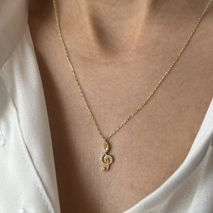 Pu&ograve; includere: Una collana con catena dorata con un piccolo ciondolo a forma di chiave di violino incrostato con pietre di zircone cubico trasparenti.