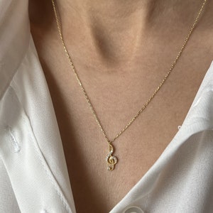 Pu&ograve; includere: Una collana con catena dorata con un piccolo ciondolo a forma di chiave di violino decorato con pietre di zircone cubico trasparenti.