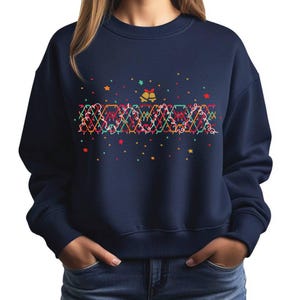 Puede incluir: Sudadera azul marino con un diseño festivo. El gráfico presenta una cadena de luces de colores, estrellas y campanas. El diseño es en tonos de rojo, verde, amarillo y naranja, creando un alegre tema navideño.