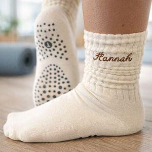 Puede incluir: Calcetines de yoga color crema, acanalados, con suela antideslizante con puntos. El calcetín derecho presenta el nombre "Hannah" bordado en escritura marrón. Diseñados para mayor comodidad y agarre durante yoga o Pilates.