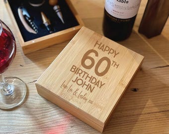 May include: A bamboo box with the text "HAPPY 60TH BIRTHDAY JOHN Love Lee & Lesley xxx" is displayed. A wine bottle, a wine glass, and a wooden box containing wine tools are also visible. The box is a gift for a 60th birthday.