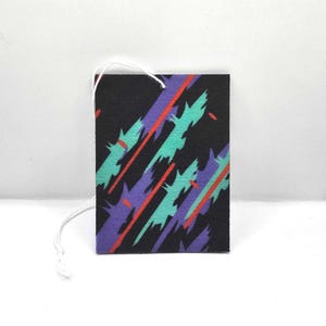 May include: A black car air freshener with a geometric pattern in shades of purple, teal, and red.