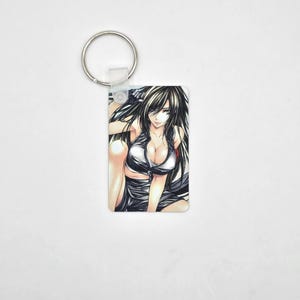 May include: A rectangular keyring with an anime-style illustration of a woman with long black hair. The woman is wearing a silver and black outfit. The keyring has a silver metal ring attached.