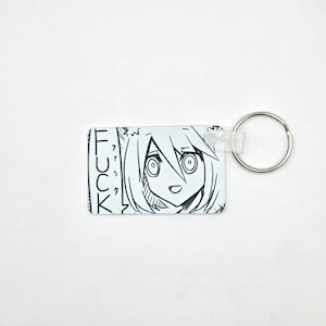 Peut inclure: Un porte-clés rectangulaire avec une illustration en noir et blanc de style anime d'un personnage et le mot "FUCK" en texte vertical. Il est équipé d'un anneau en métal argenté.