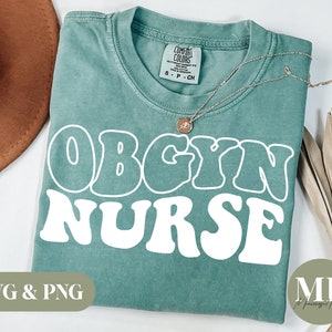 May include: A teal blue t-shirt with the text "OBGYN NURSE" in white retro-style lettering. The shirt is folded and lying on a white surface.