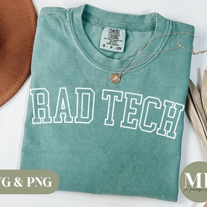 Könnte beinhalten: Ein blaugrünes T-Shirt mit dem Text "RAD TECH" in weißen umrandeten Buchstaben. Das Shirt liegt flach auf einer weißen Oberfläche.