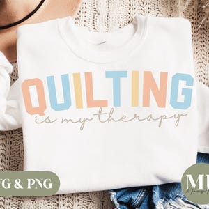 May include: White sweatshirt with the text "QUILTING is my therapy" in rainbow colors. The text is in a bold, blocky font.