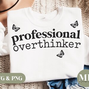 May include: White sweatshirt with black text that reads "professional overthinker" and black butterfly graphics.