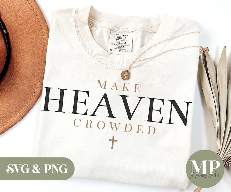 Pu&ograve; includere: Una maglietta bianca con il testo "MAKE HEAVEN CROWDED" in lettere nere e marroni. Una piccola croce si trova sotto il testo. La maglietta &egrave; su uno sfondo bianco con un cappello marrone e una pianta secca.