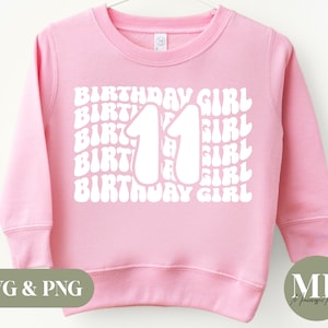 Op de afbeelding: Roze sweatshirt met een wit grafisch ontwerp met de tekst "Birthday Girl" en het nummer "11" in een retro-lettertype.