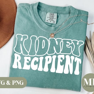 May include: A teal green t-shirt with the words "Kidney Recipient" in white retro-style lettering.