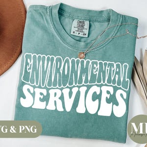 Puede incluir: Una camiseta verde azulada con el texto "ENVIRONMENTAL SERVICES" en blanco, con letras de estilo retro. La camiseta está hecha de un material suave y cómodo y es perfecta para el uso diario.