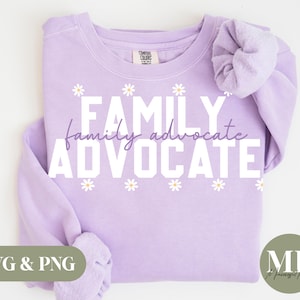 Puede incluir: Sudadera morada con el texto "FAMILY family advocate ADVOCATE" en letras blancas con pequeñas flores blancas de margarita alrededor del texto.