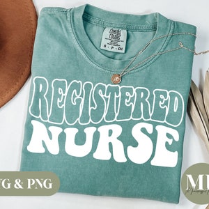 May include: A teal blue t-shirt with the text "REGISTERED NURSE" in white, retro-style lettering. The shirt is folded and laid flat on a white surface.