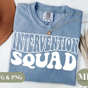 May include: A light blue t-shirt with the text "Intervention Squad" in white, retro-style lettering. The shirt is made of a soft, comfortable material and has a distressed look.