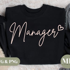 May include: Black crew neck sweatshirt with the word "Manager" in a light pink script font, with a heart symbol at the end. The bottom left corner has the text "SVG & PNG" in a green box.